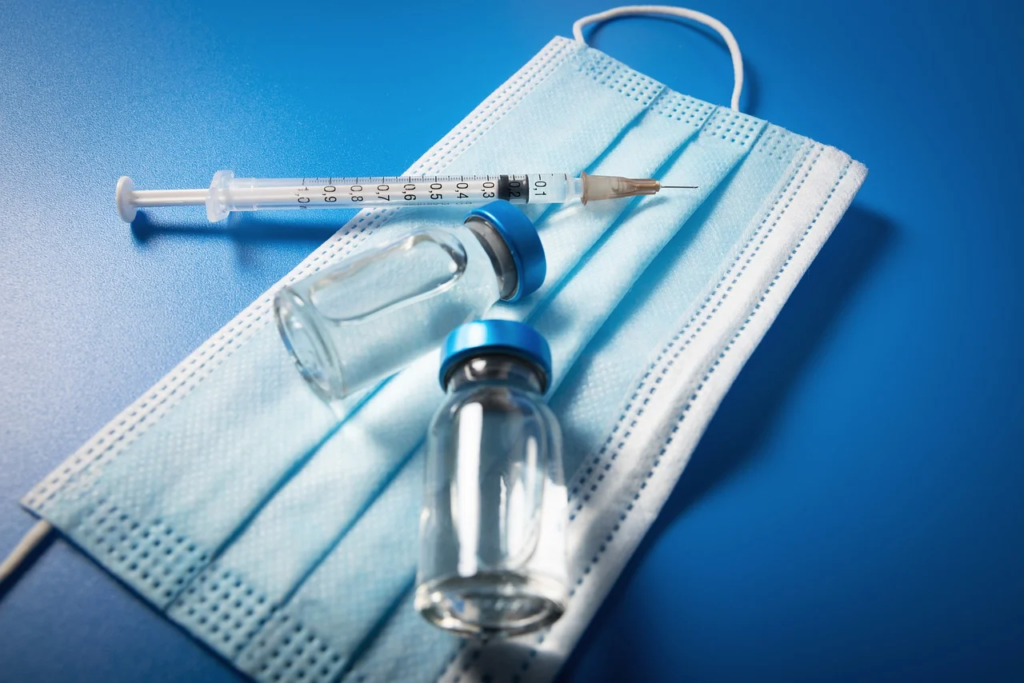 Pots de vaccins à côté d'une seringue et d'un masque.